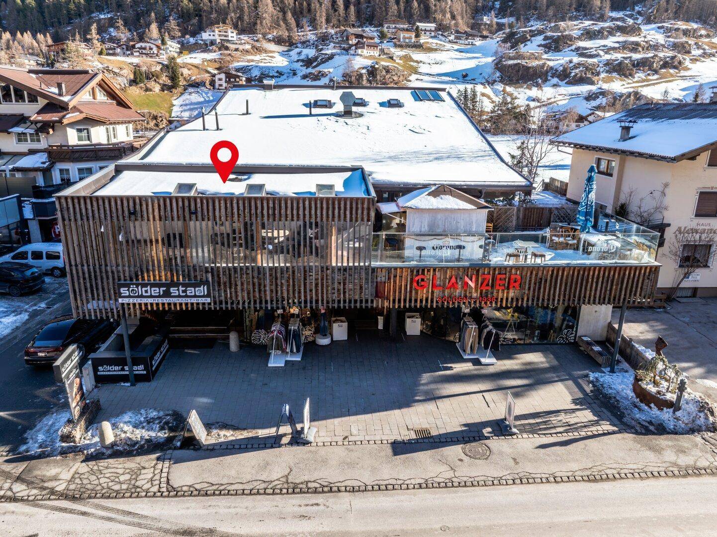 Nahaufnahme des Gebäudes mit markanter Holzlamellenfassade und einer möblierten Terrasse im ersten Stock, umgeben von Schnee.