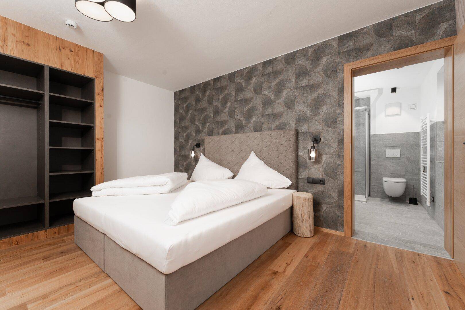 Gemütliches Schlafzimmer mit Doppelbett, Holzboden und offenem Kleiderschrank, mit Zugang zum Badezimmer.