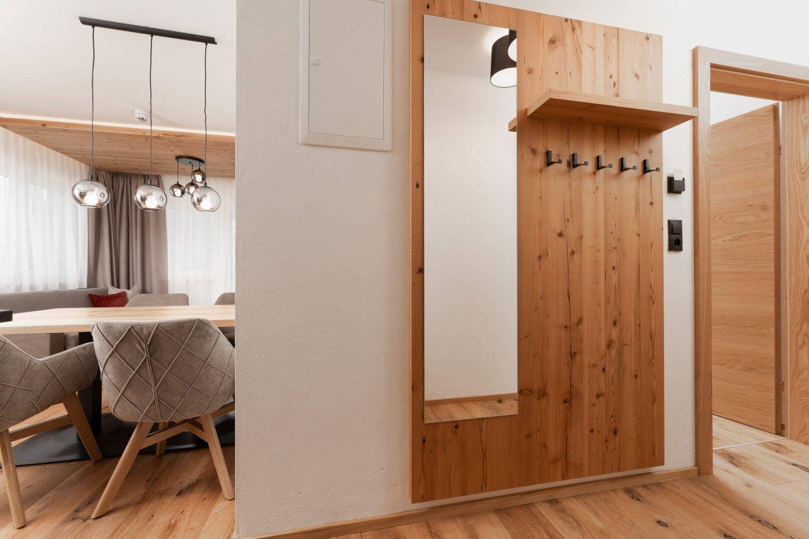 Heller Eingangsbereich mit Holzboden, großem Spiegel und Garderobe, der zum Wohnbereich führt.