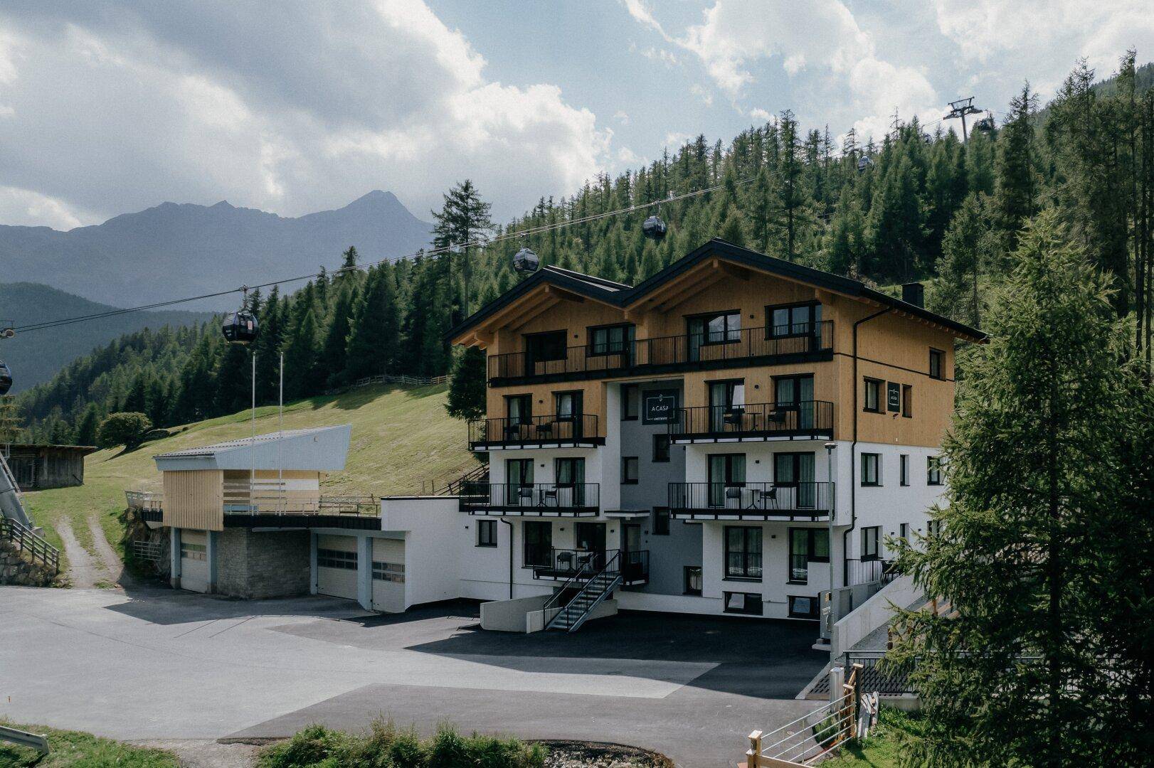 Das moderne Apartmenthaus fügt sich harmonisch in die alpine Landschaft ein, mit Bergblick und Seilbahnen.