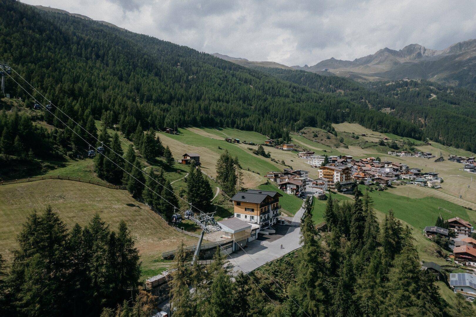 Weitläufige Luftaufnahme des Apartmenthauses mit Blick auf das Tal, ein Dorf und die umliegenden Berge.