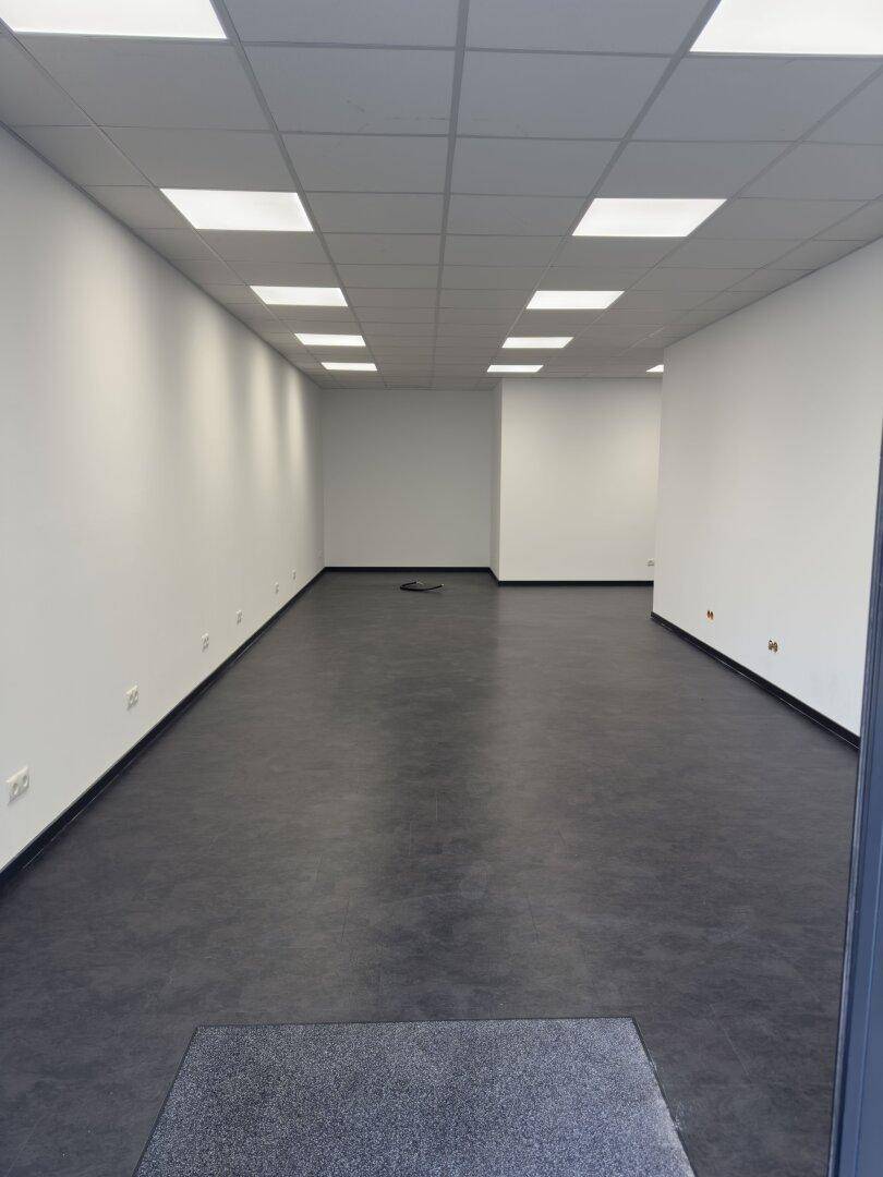 Heller und leerer Gewerberaum mit dunklem Vinylboden und moderner Deckenbeleuchtung.