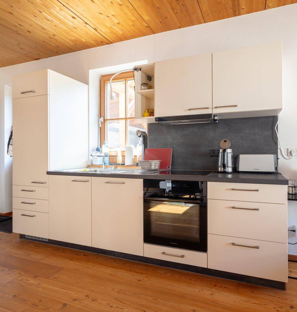 Moderne Einbauküche mit hellen Schränken, dunkler Arbeitsplatte und Fenster für Tageslicht.