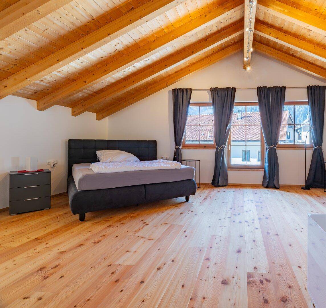 Großes Schlafzimmer im Dachgeschoss mit sichtbaren Holzbalken, Holzboden und viel Platz.