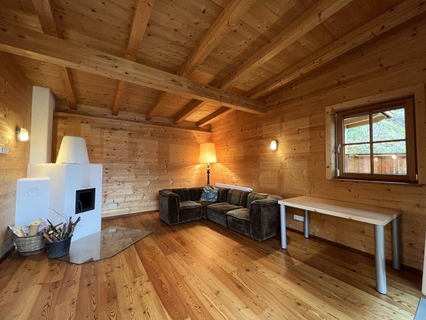 Rustikales Wohnzimmer mit Holzwänden, Holzboden und Kaminofen, strahlt Gemütlichkeit aus.
