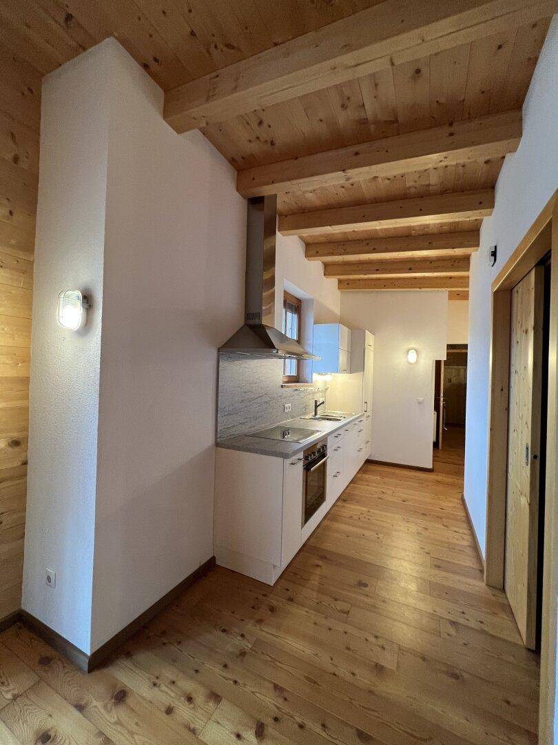 Moderne Küchenzeile mit hellen Schränken, Dunstabzugshaube und Holzboden im Landhausstil.