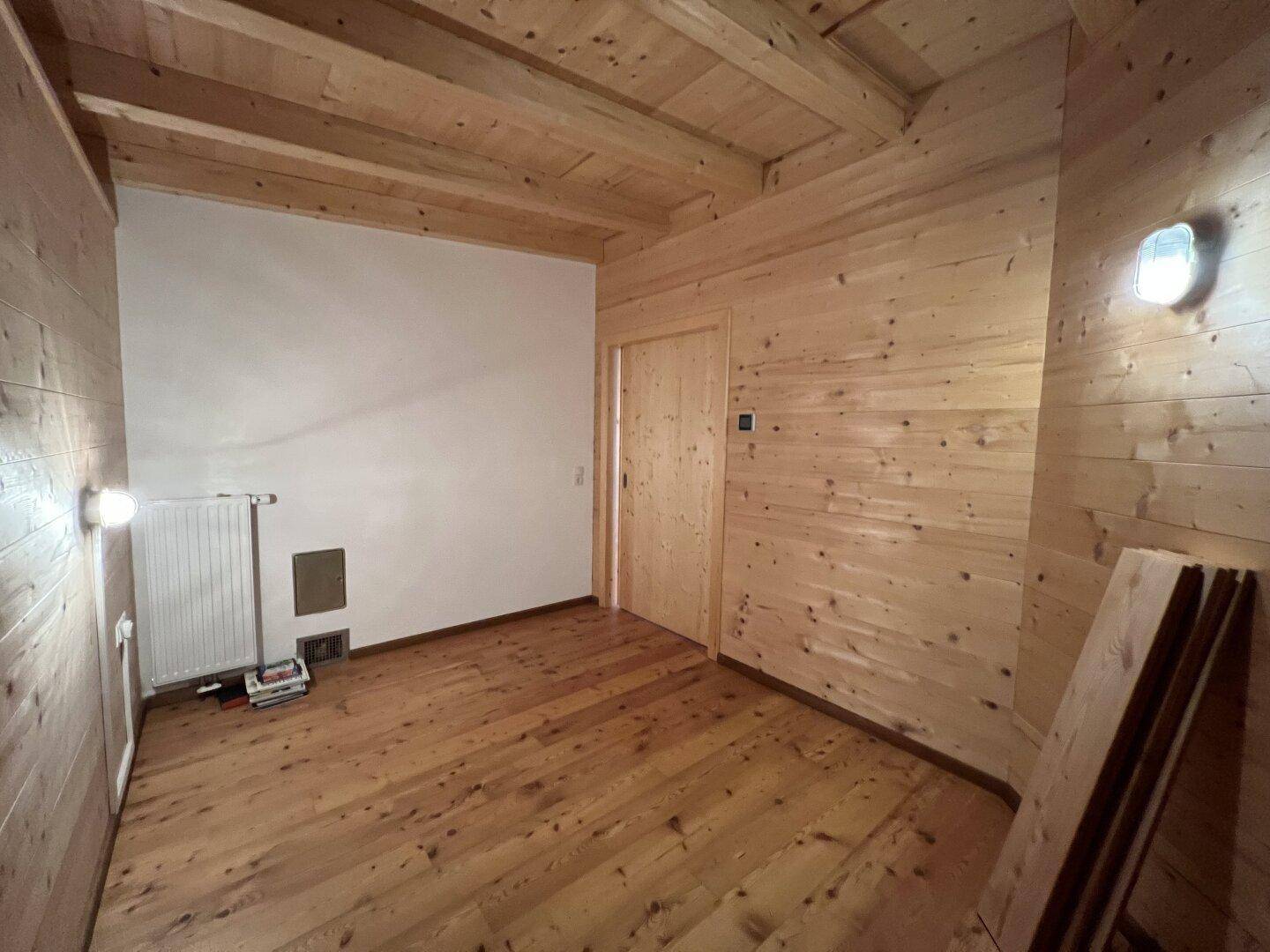 Schlafzimmer mit Holzwänden, Holzboden und Heizkörper, bereit zur individuellen Gestaltung.