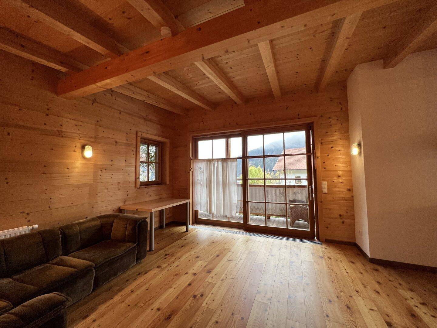 Wohnzimmer mit Holzwänden, Holzboden und Zugang zu einem Balkon mit Bergblick.