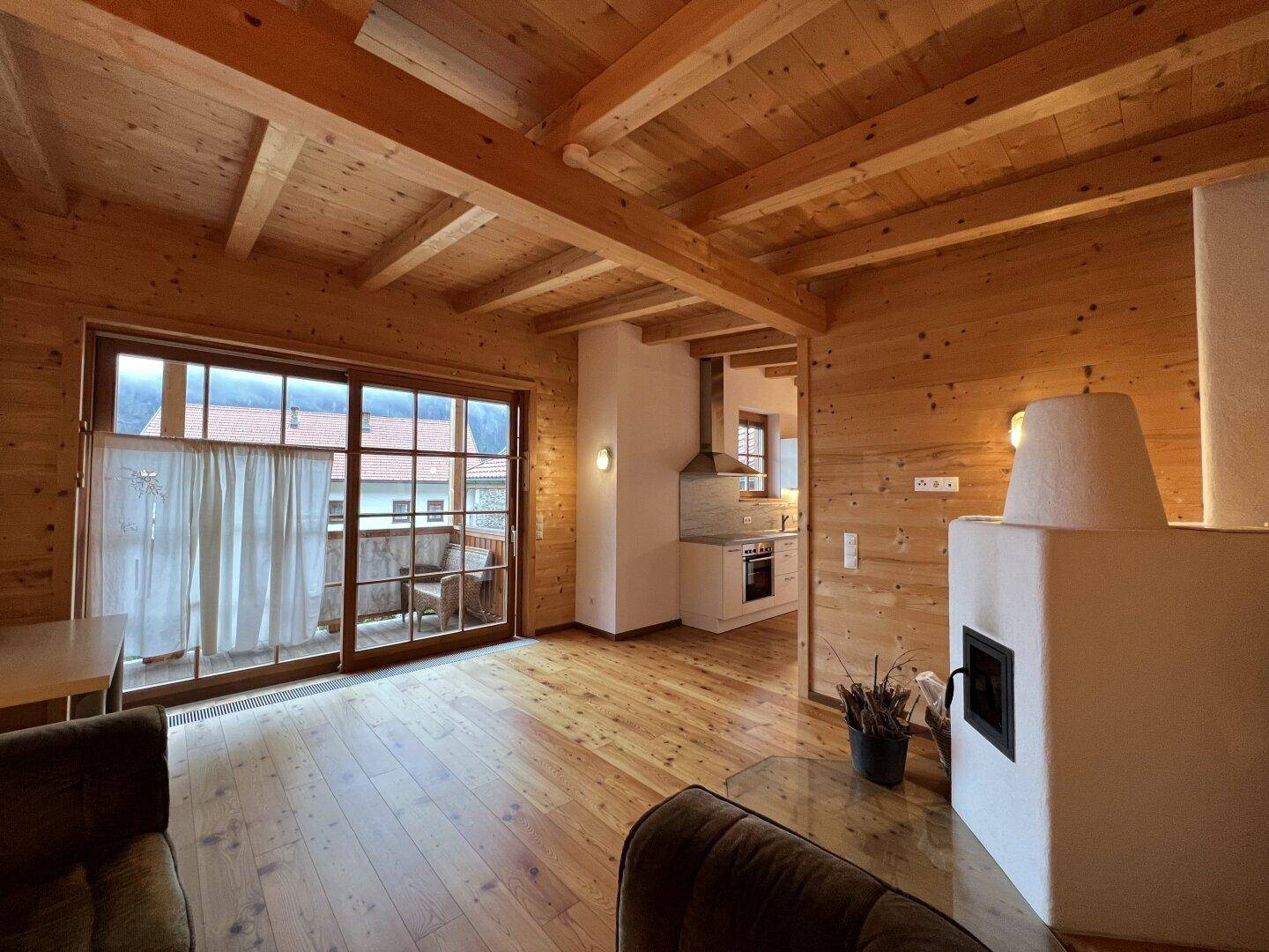 Offener Wohn-Essbereich mit Kaminofen, Holzboden und Zugang zum Balkon.