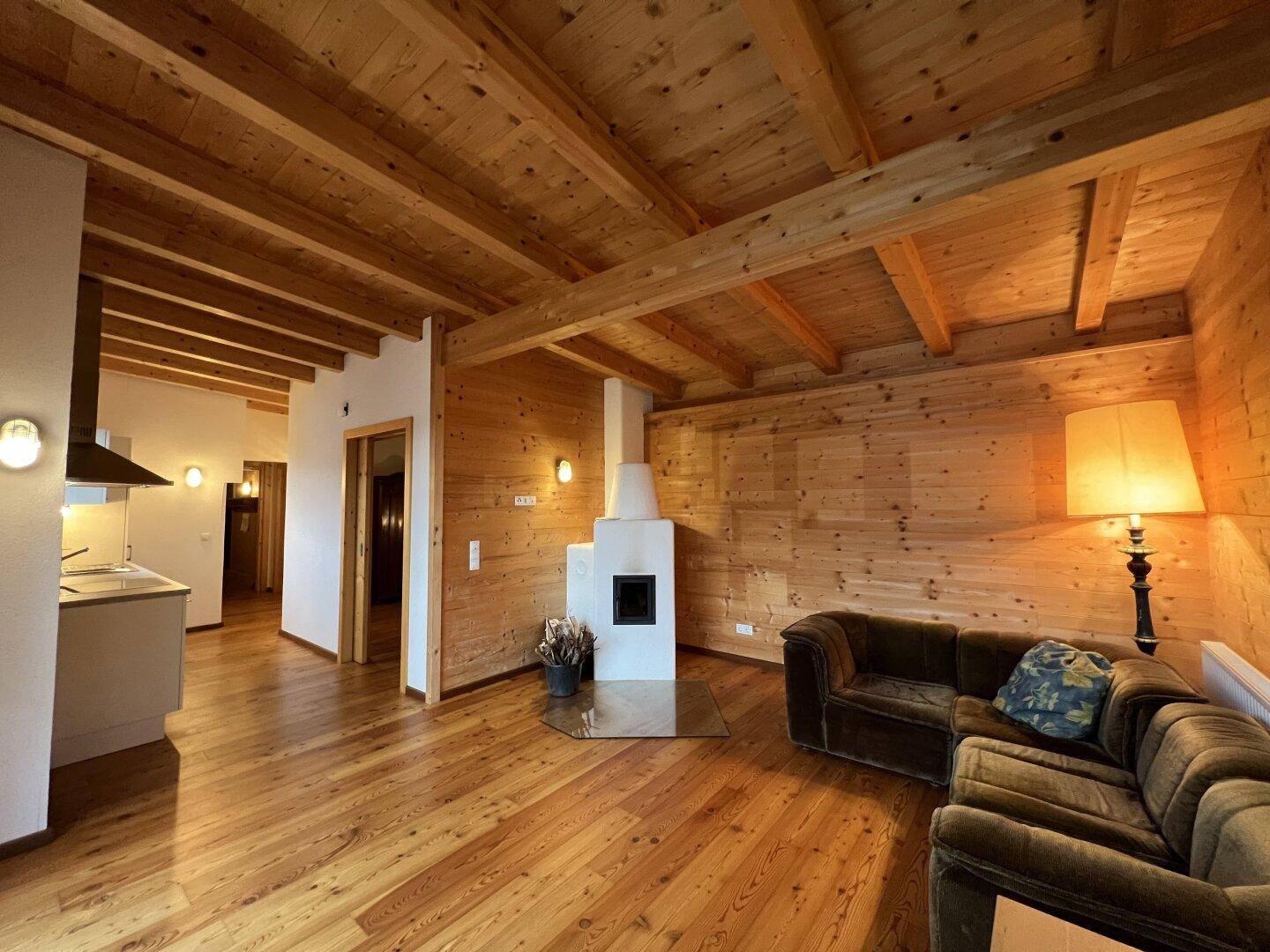 Gemütlicher Wohnbereich mit Holzwänden, Holzboden und Kaminofen, offen zur Küche.