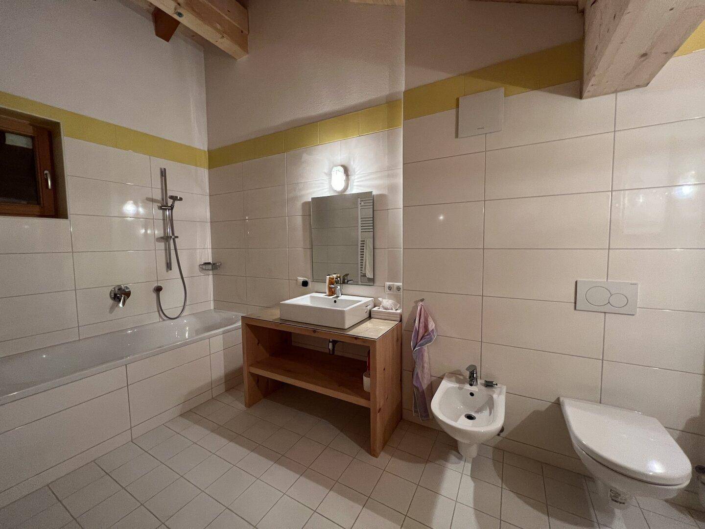 Helles Badezimmer mit Badewanne, Bidet und WC, ausgestattet mit einem Heizkörper.