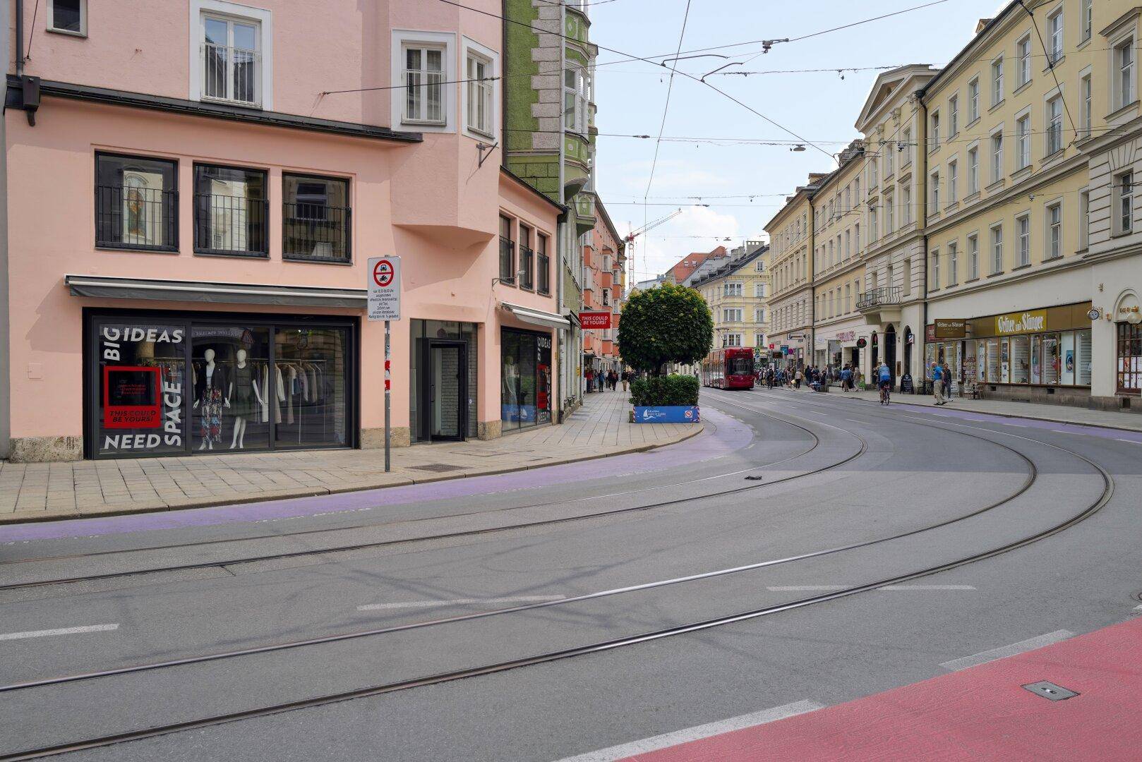 Blick auf eine belebte Stadtstraße mit historischen Gebäuden, Straßenbahnschienen und Passanten.