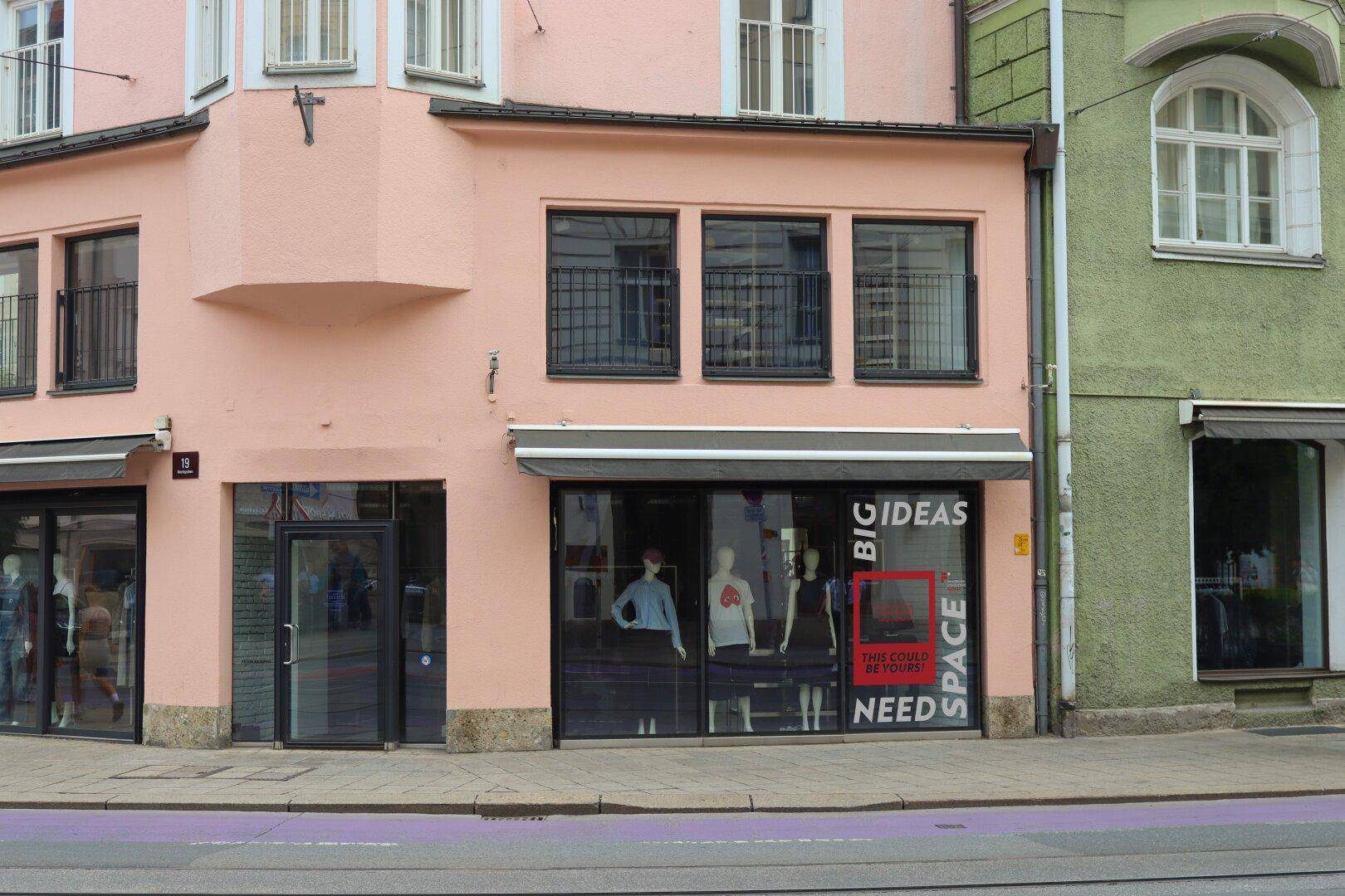 Nahaufnahme der Ladenfront eines rosa Gebäudes mit großen Schaufenstern und Eingangsbereich.