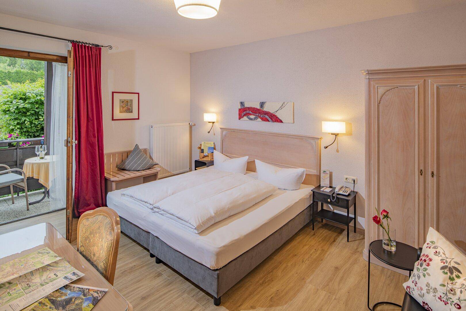 Helles Schlafzimmer mit Doppelbett, Laminatboden und direktem Zugang zu einem kleinen Balkon.