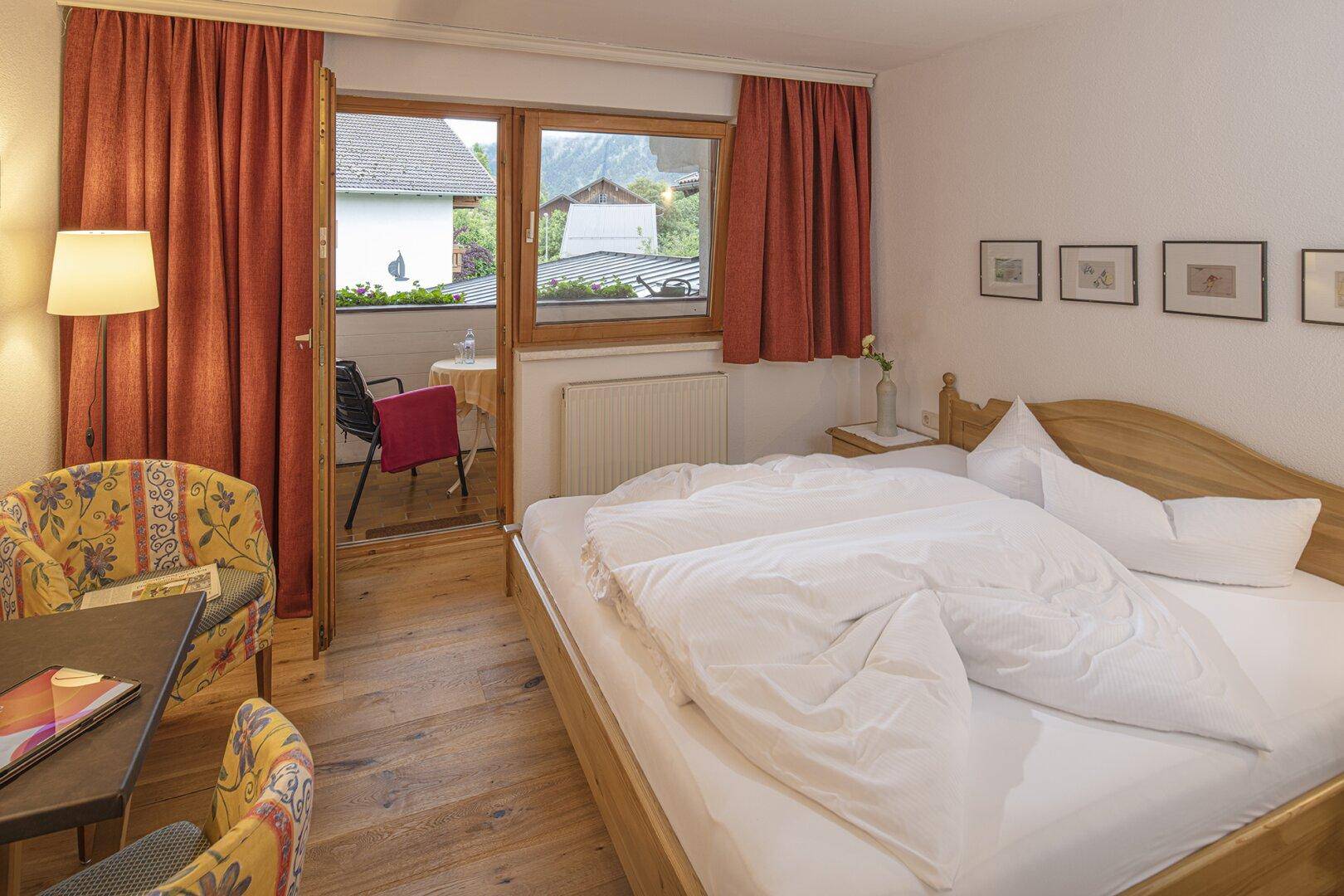 Gemütliches Schlafzimmer mit Holzdielenboden, Doppelbett und direktem Zugang zu einem Balkon.