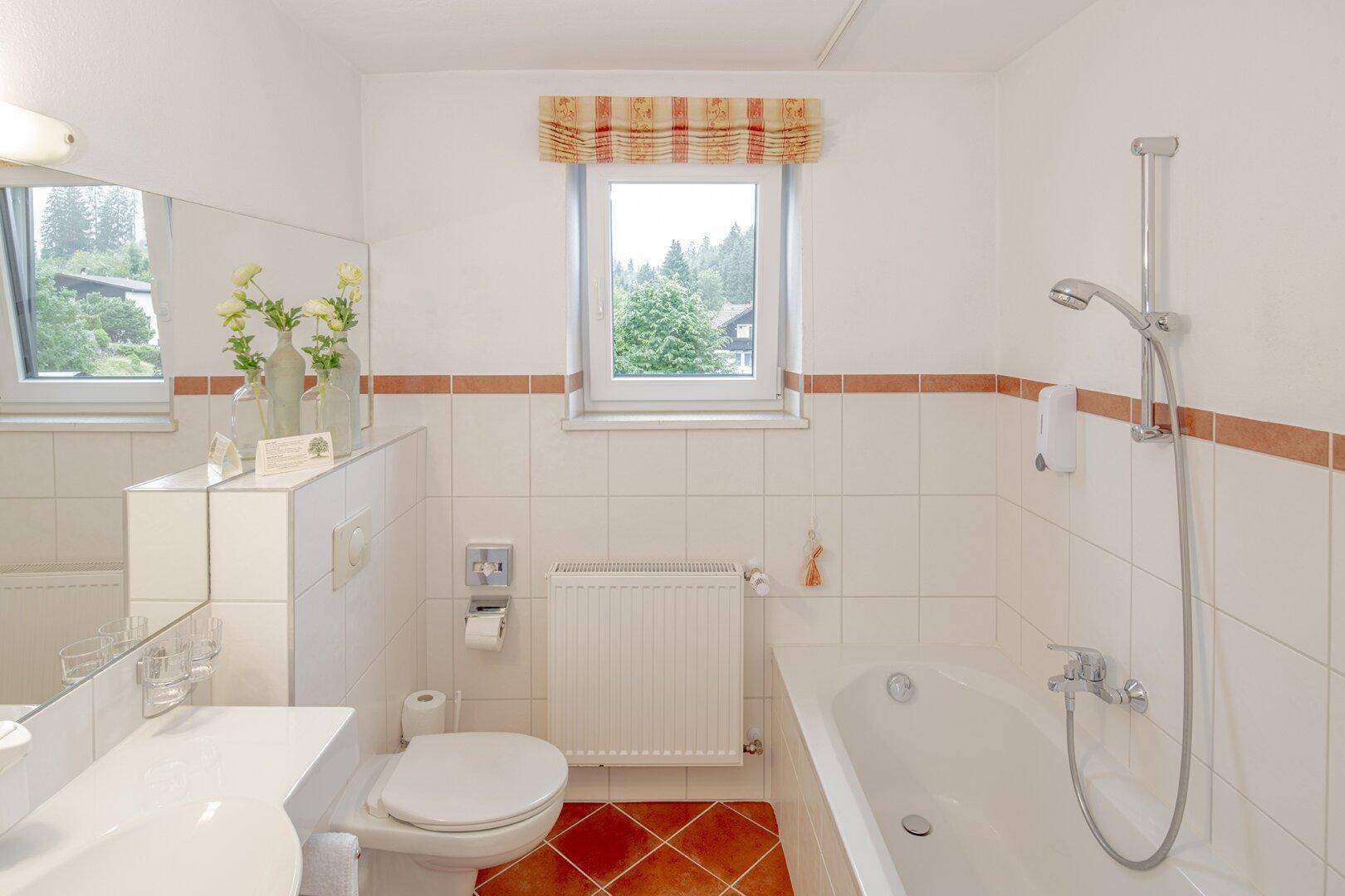 Helles Badezimmer mit Badewanne, Dusche, WC und einem Fenster für natürliches Tageslicht.