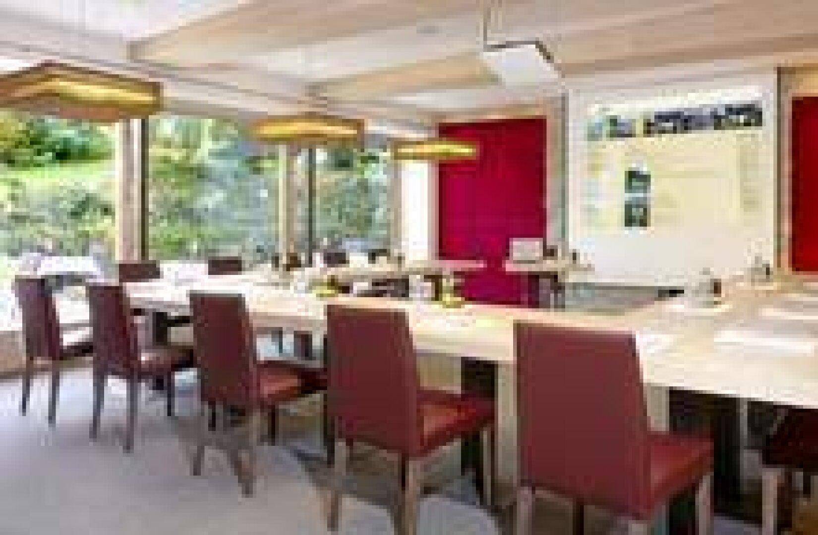 Großer Konferenzraum mit langen Tischen, bequemen Stühlen und viel Tageslicht durch große Fenster.