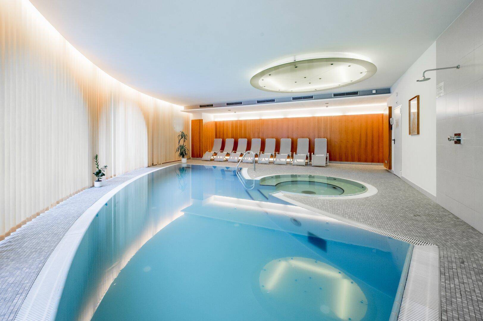 Großzügiger Innenpoolbereich mit bequemen Liegestühlen, einem Whirlpool und stimmungsvoller Beleuchtung.