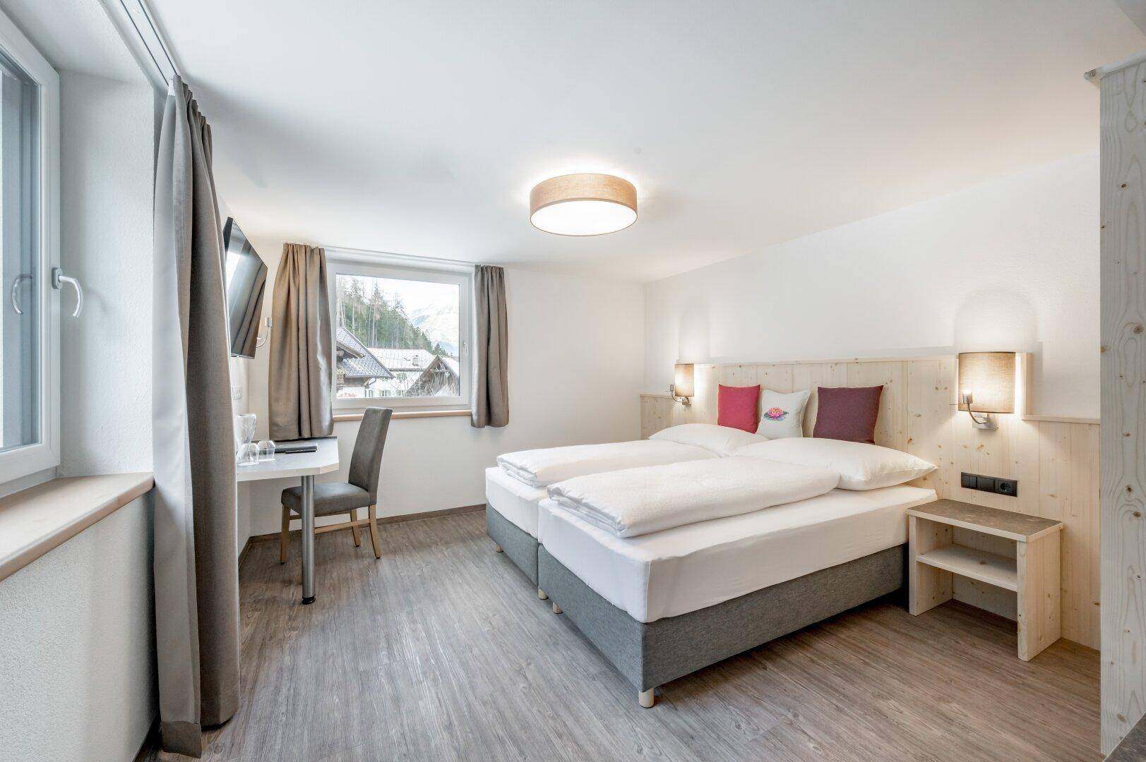 Modernes Schlafzimmer mit Doppelbett, Schreibtisch und einem Fenster, das einen Blick auf die Umgebung bietet.