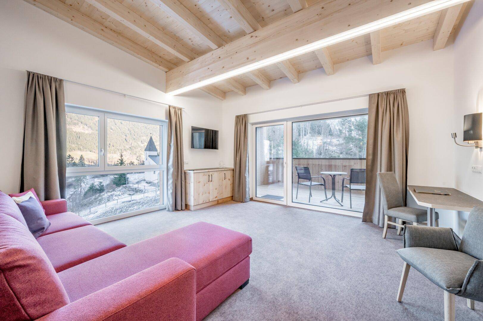 Heller Wohnbereich mit großen Fenstern, pinkem Sofa und direktem Zugang zu einem Balkon mit Sitzgelegenheiten.