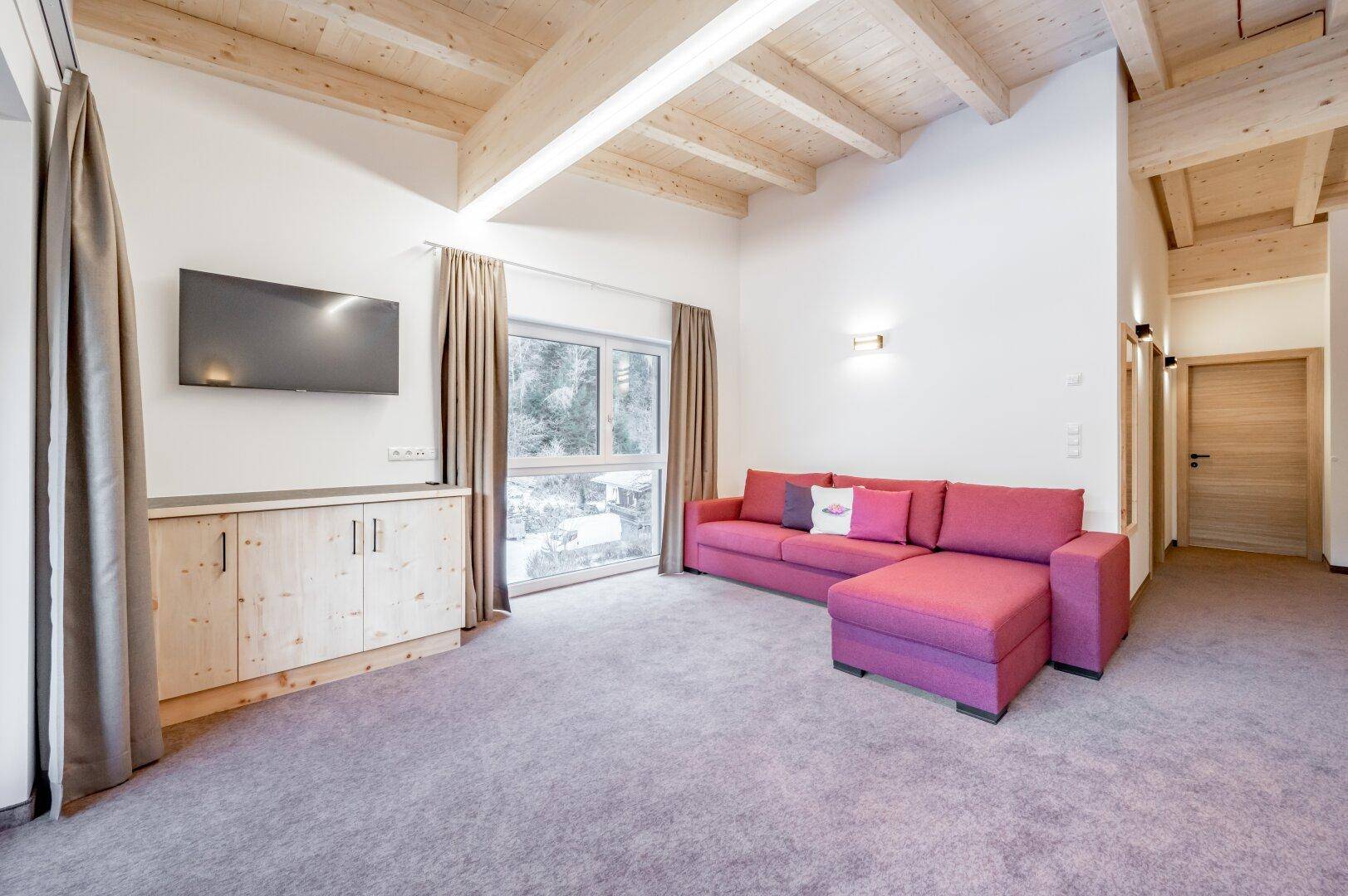 Geräumiges Wohnzimmer mit bequemer pinker Couch, Holzelementen und einem Flachbildfernseher an der Wand.