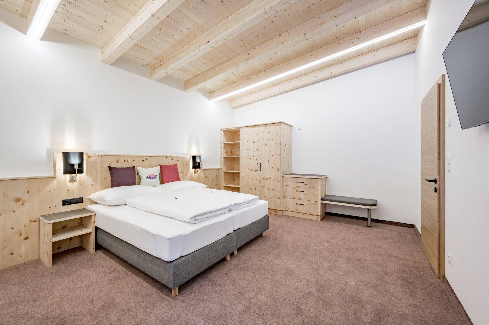 Gemütliches Schlafzimmer mit Holzbalkendecke, Doppelbett und passenden Holzmöbeln in hellem Design.