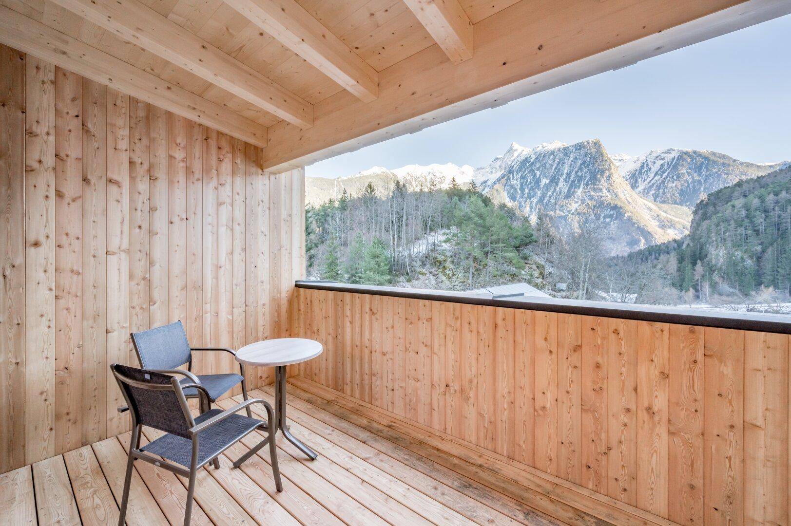 Geräumiger Holzbalkon mit Sitzgelegenheiten und einem atemberaubenden Panoramablick auf die umliegenden Berge.