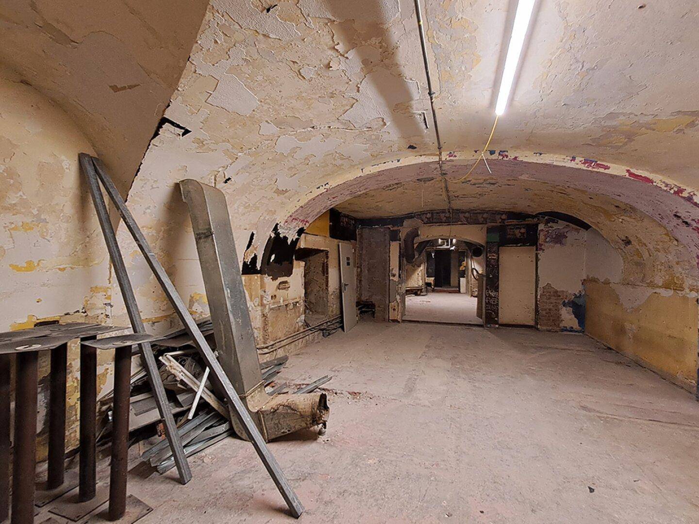 Verfallener Kellerraum mit gewölbter Decke und sichtbaren Rohren, bereit zur Renovierung.