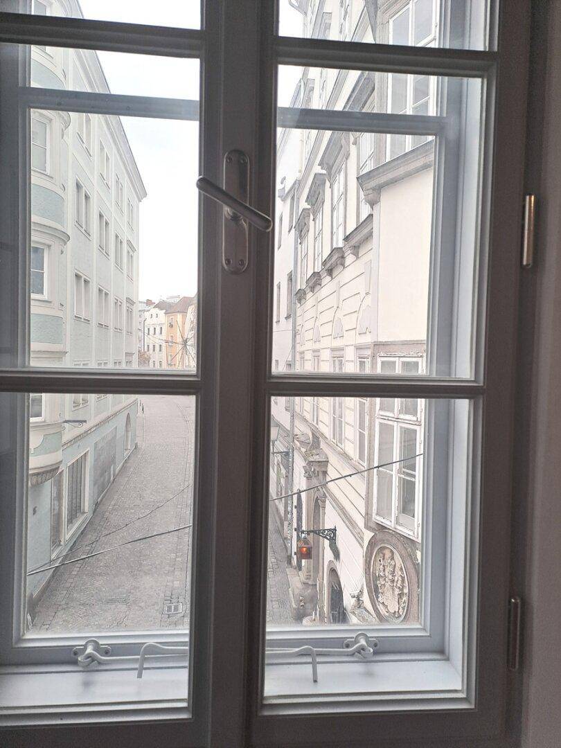 Blick aus einem Fenster auf eine historische Gasse mit Kopfsteinpflaster und alten Gebäuden.