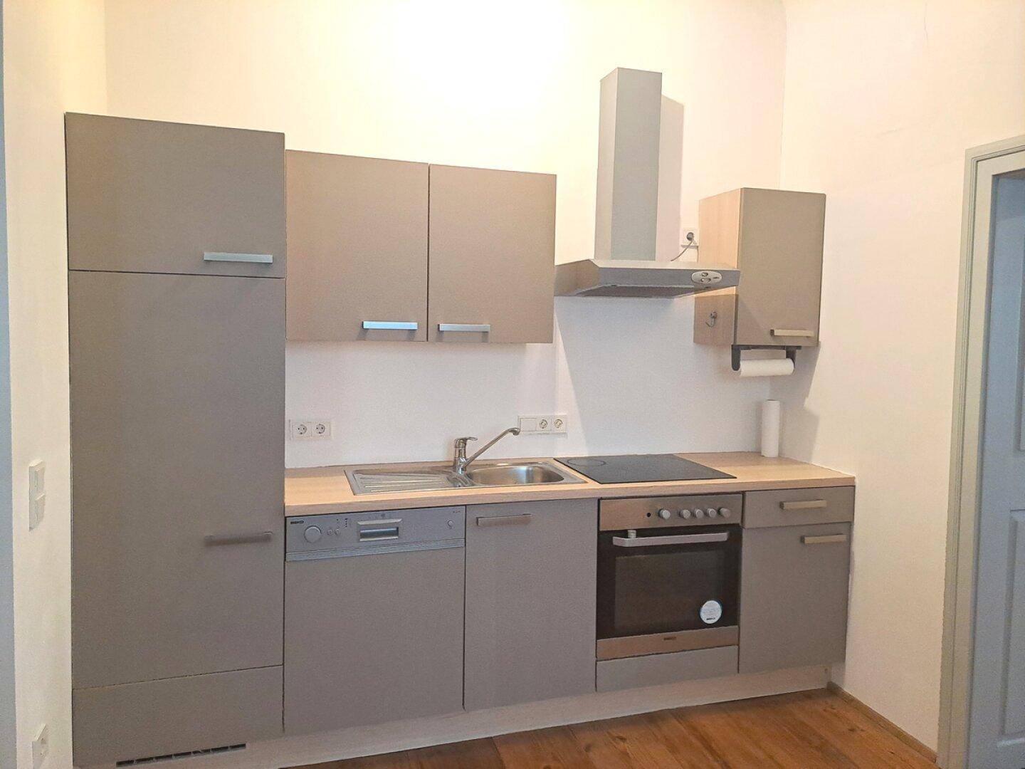 Funktionale Einbauküche in Grau mit integrierten Geräten, Induktionskochfeld und Dunstabzugshaube.