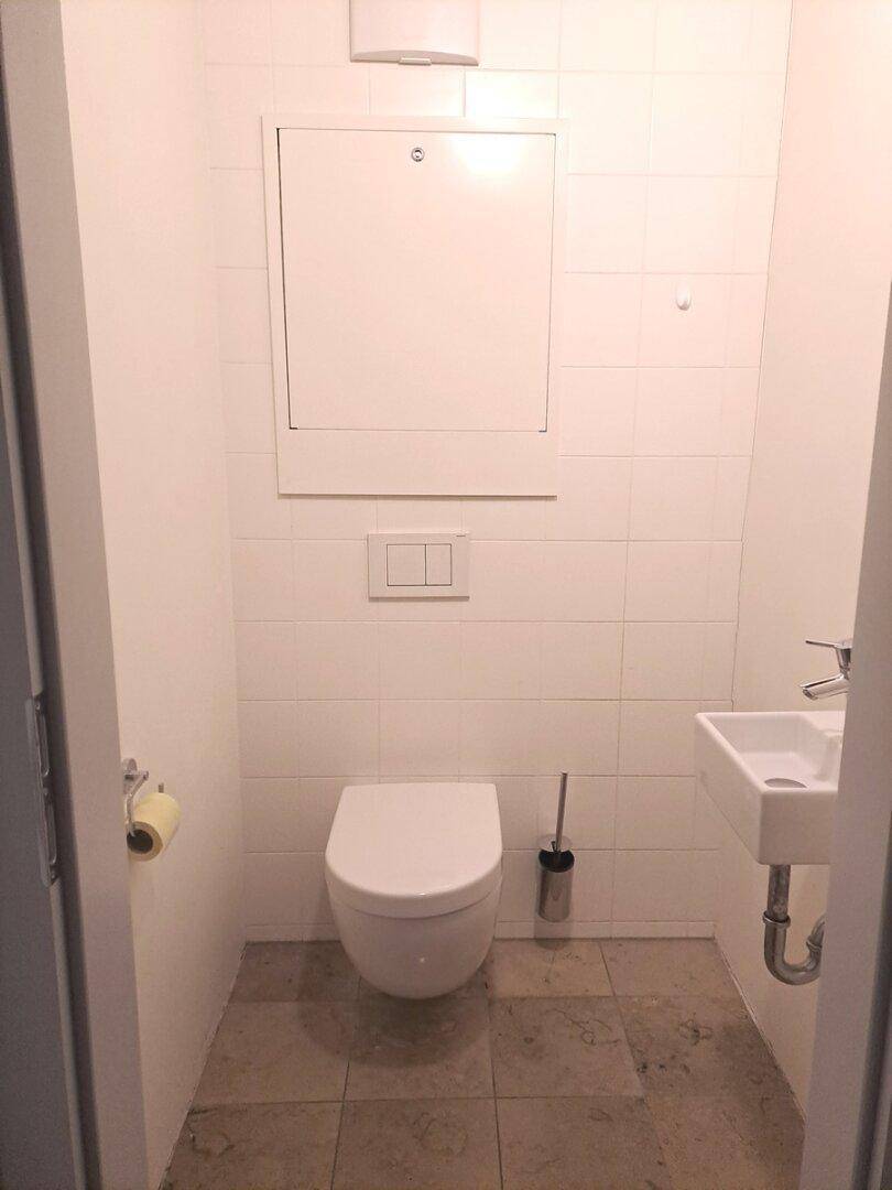 Kleines Gäste-WC mit Wand-WC, Waschbecken und hellen Fliesen.