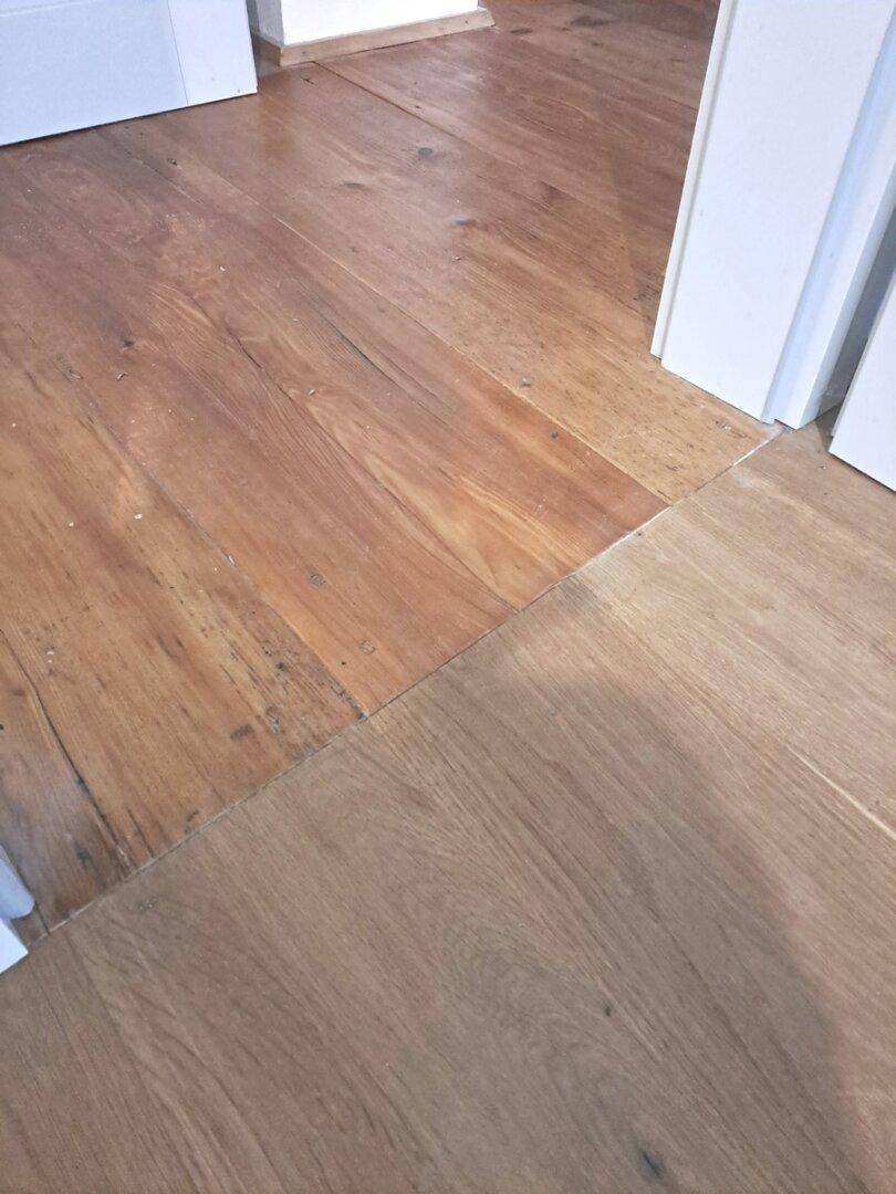 Detailaufnahme von zwei verschiedenen Holzdielenböden, die an einer Türschwelle aufeinandertreffen.