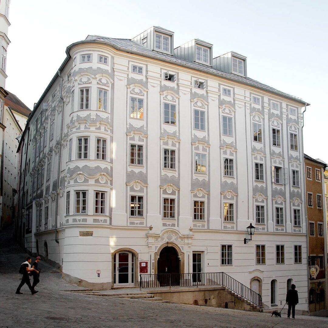 Historisches Eckgebäude mit eleganter Fassade, vielen Fenstern und Mansarddach in einer Stadtgasse.