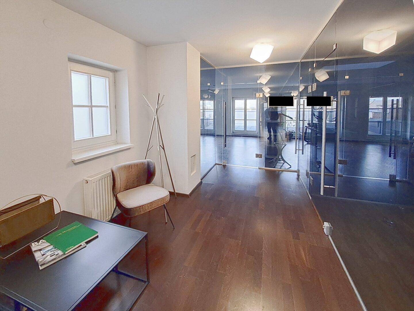 Eingangsbereich eines Büros mit dunklem Holzparkett, großen Fenstern und modernen Glasabtrennungen.