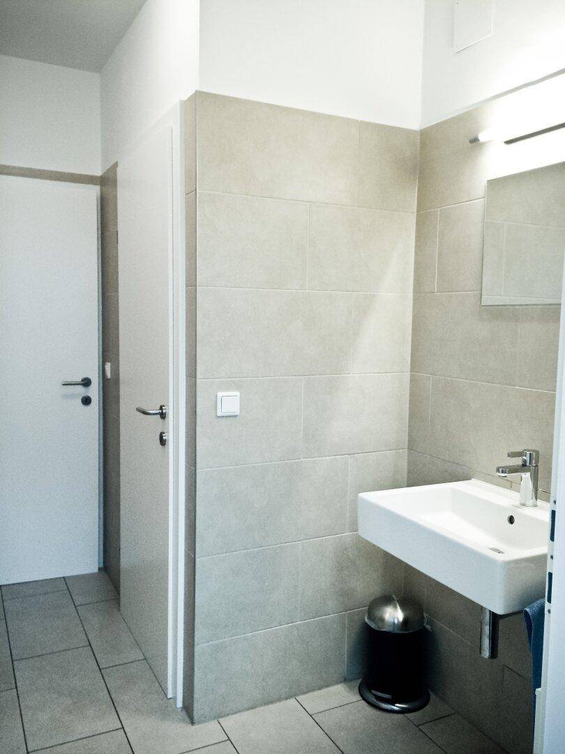 Modernes Badezimmer mit hellgrauen Fliesen an Wänden und Boden sowie einem schwebenden Waschbecken.