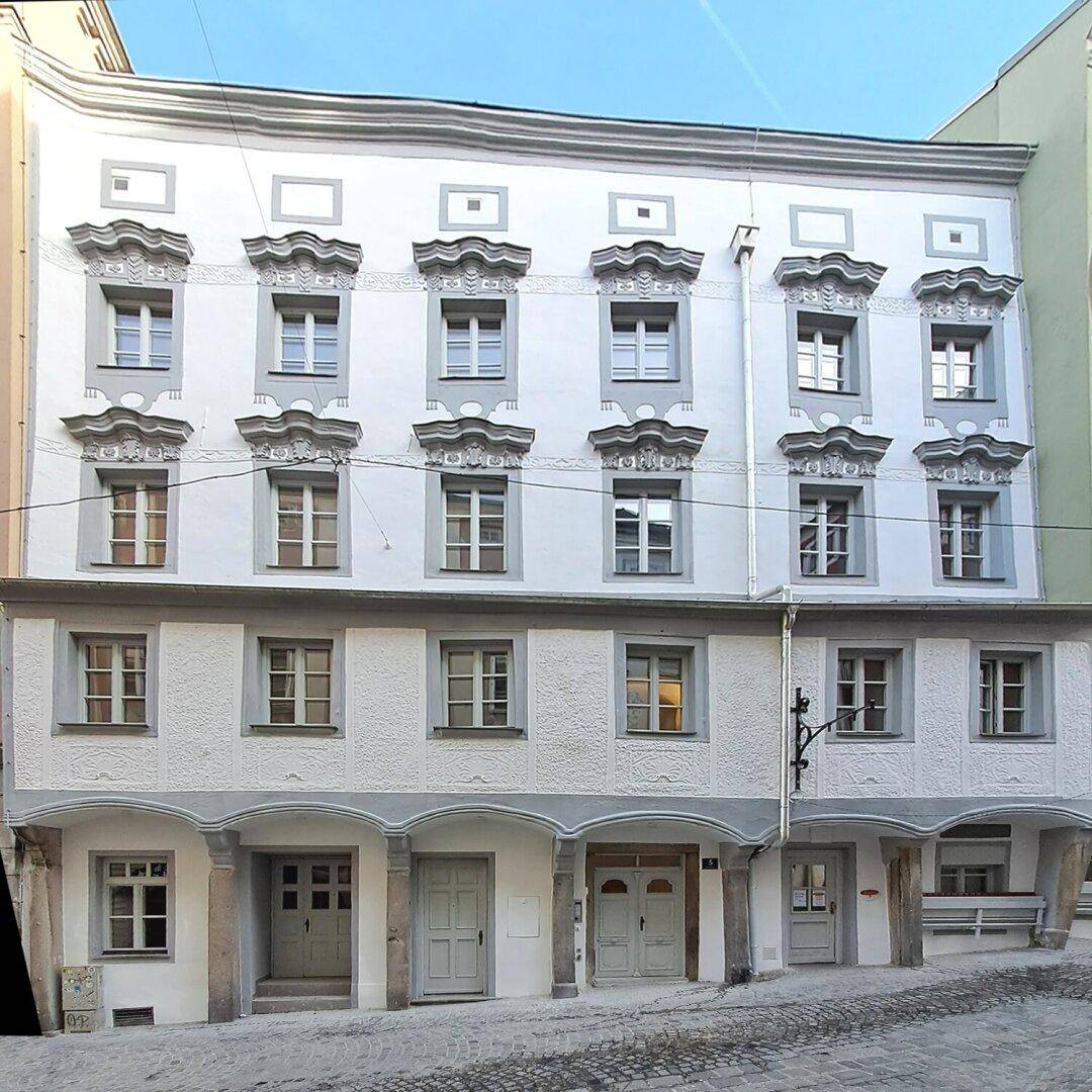 Historische Fassade eines Gebäudes mit kunstvollen Fensterrahmen und traditioneller Architektur in einer Gasse.