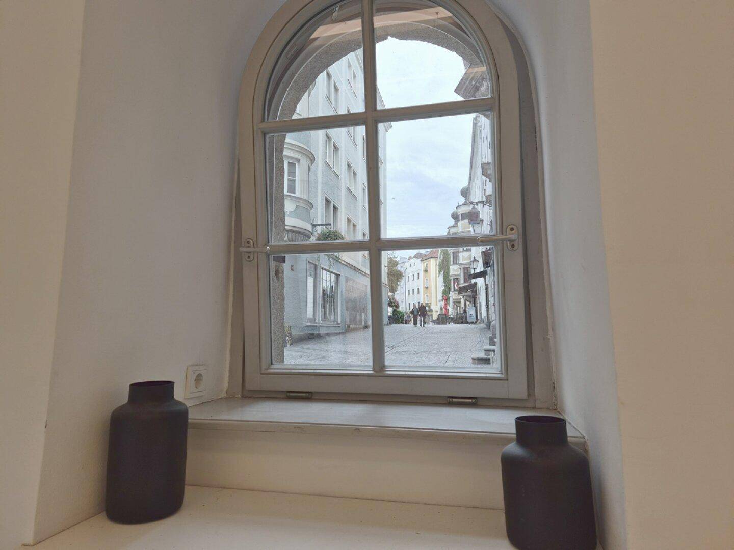 Rundbogenfenster mit Blick auf eine belebte historische Straße und gegenüberliegende Gebäude.
