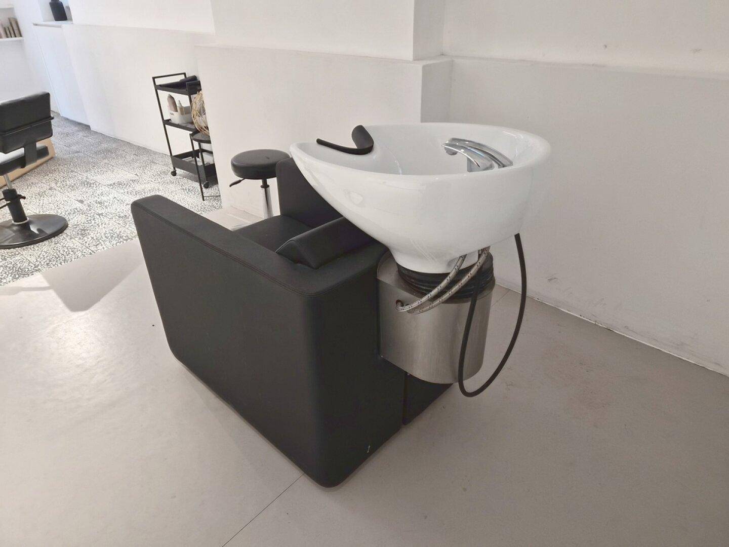 Detailansicht eines schwarzen Friseurstuhls mit integriertem Waschbecken in einem hellen Salon.