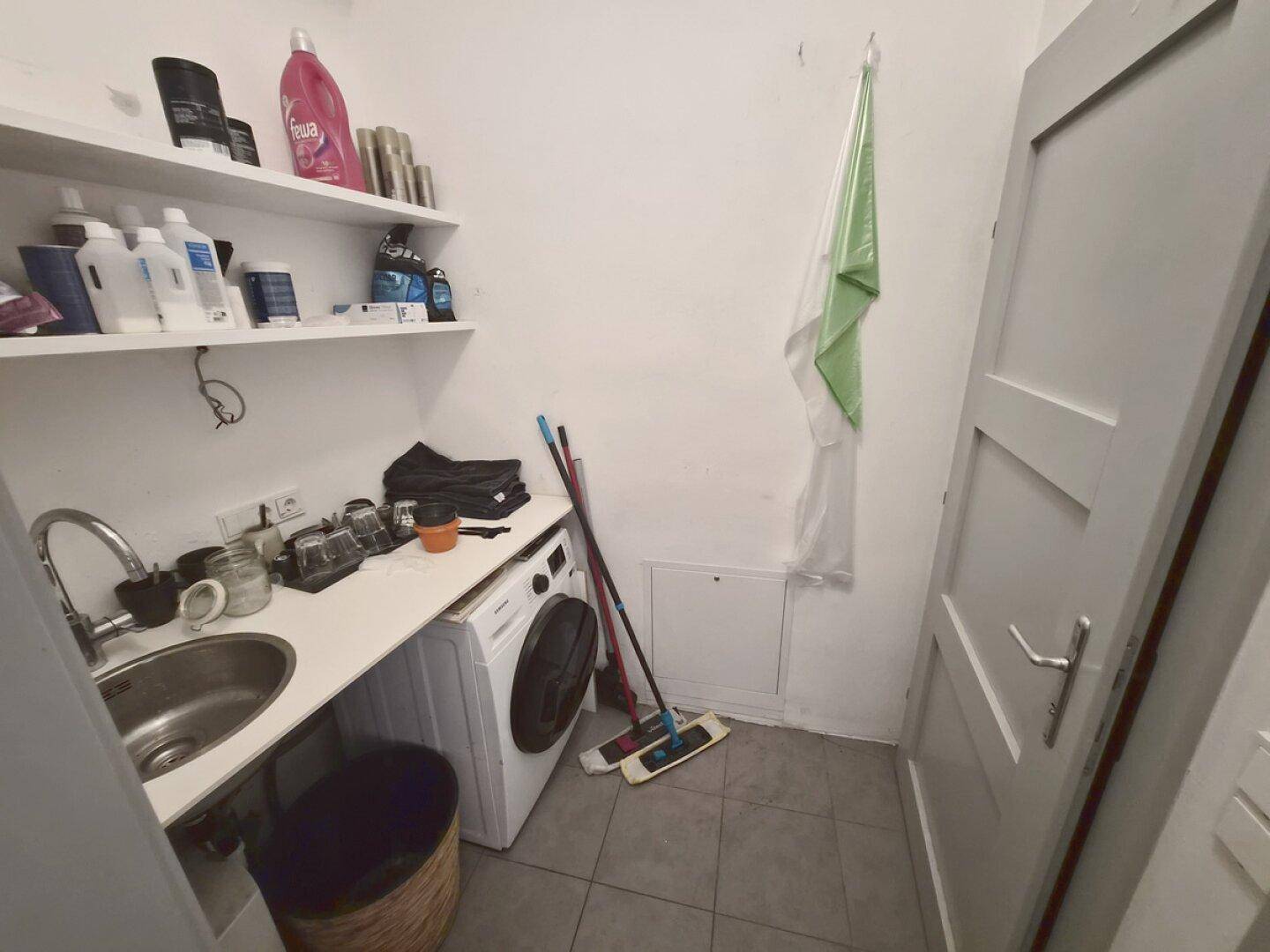 Praktischer Waschraum mit Waschmaschine, Spülbecken, Regalen und Fliesenboden.