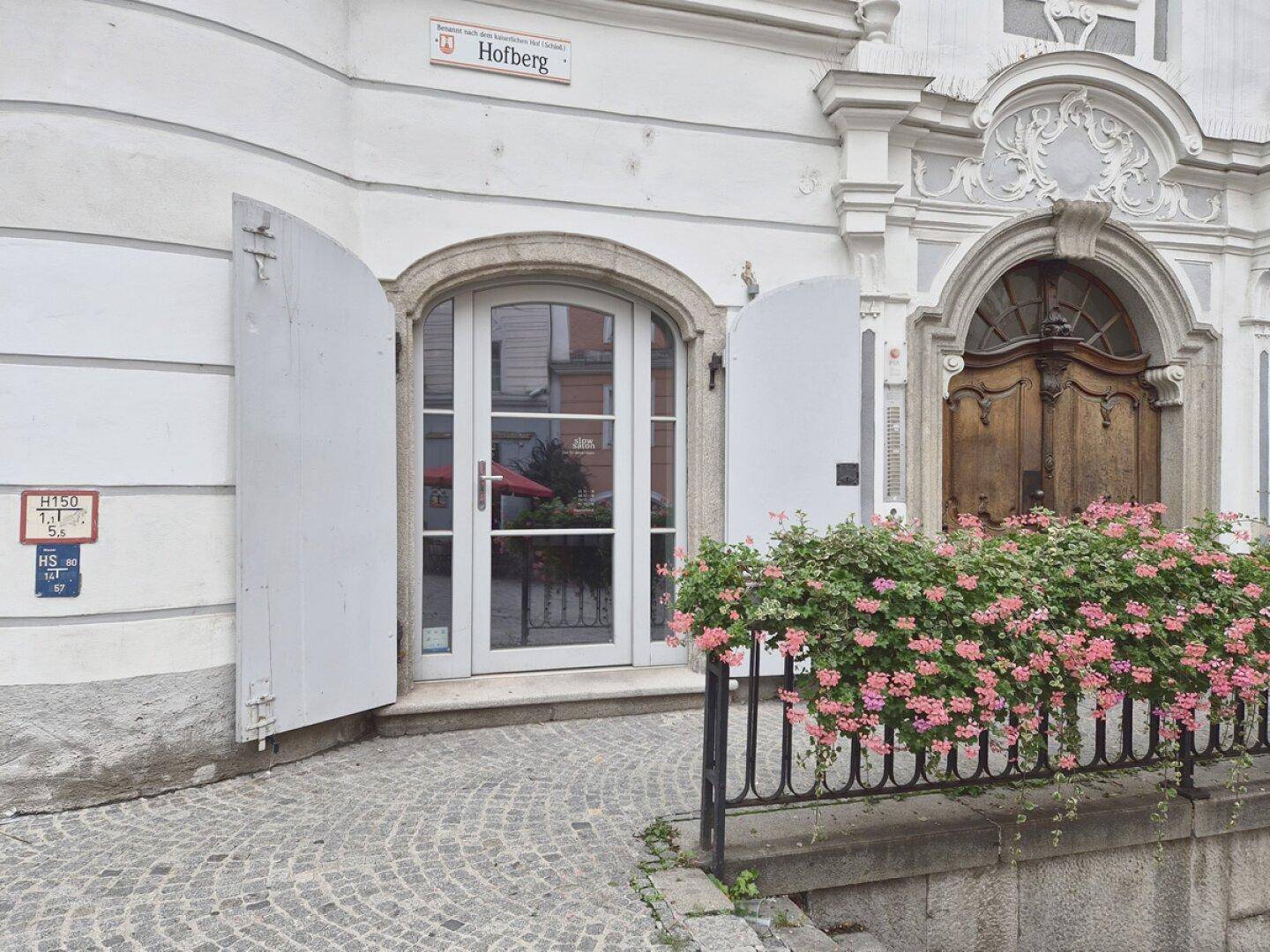 Historischer Gebäudeeingang mit Holztür, Blumenkästen und Kopfsteinpflaster in einer Gasse.