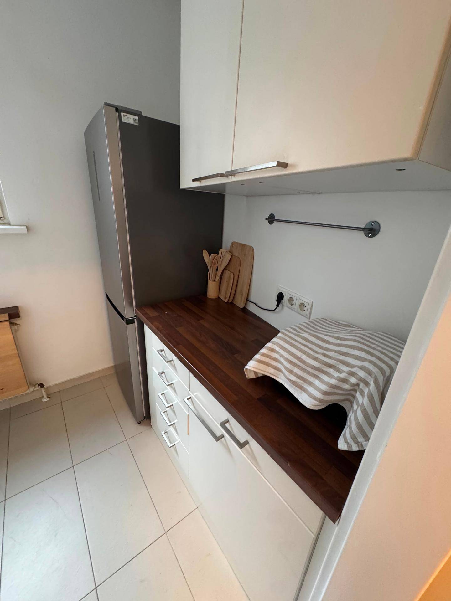 Kleine Küche mit weißen Schränken, Holz-Arbeitsplatte und Kühlschrank.