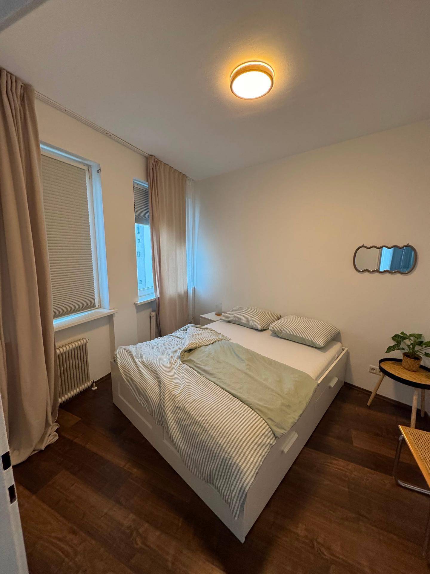 Gemütliches Schlafzimmer mit hellem Bett, Vorhängen und dunklem Holzfußboden.