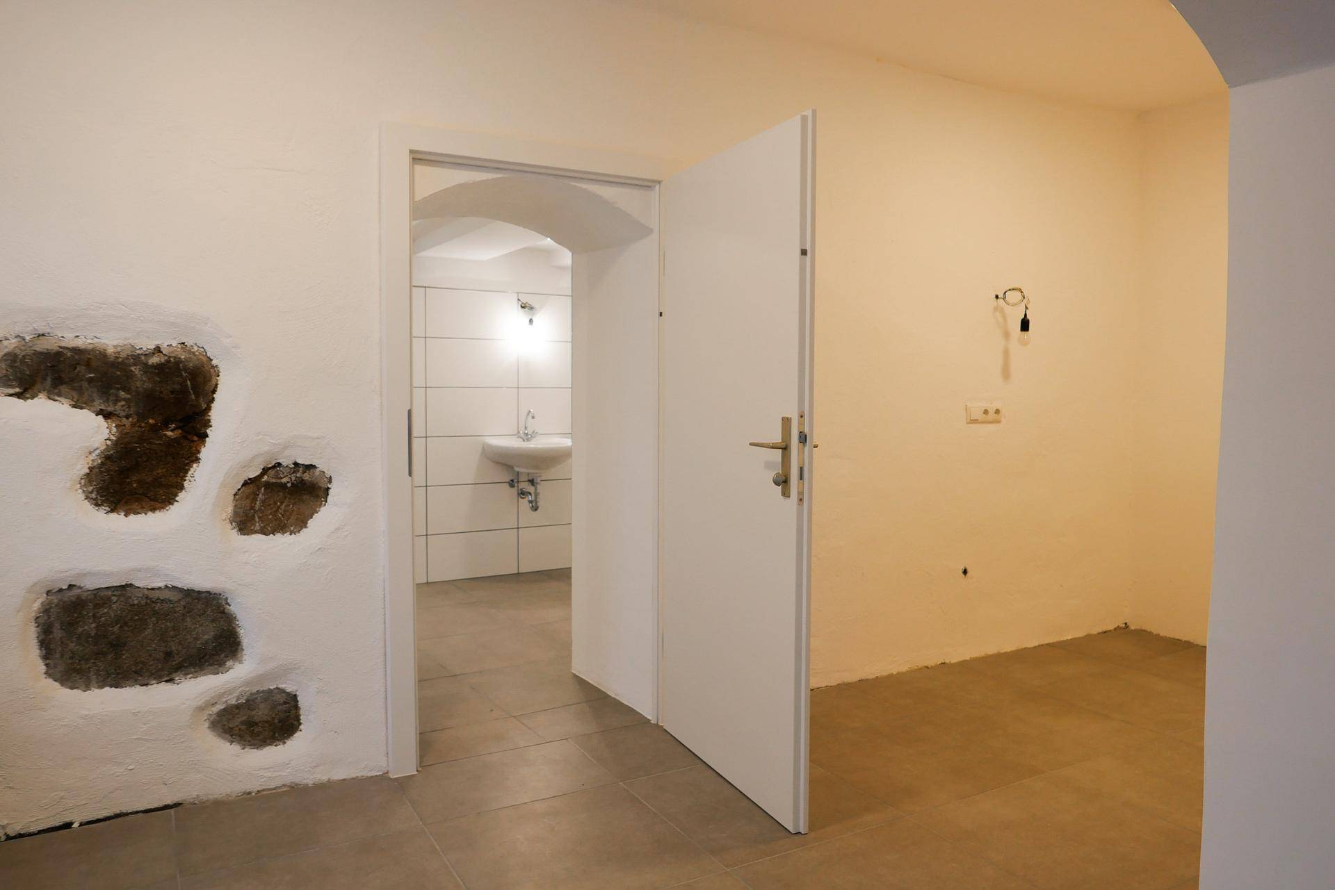 Flur mit freiliegenden Steinwänden und einem Durchgang zu einem modern gefliesten Badezimmer mit Waschbecken.