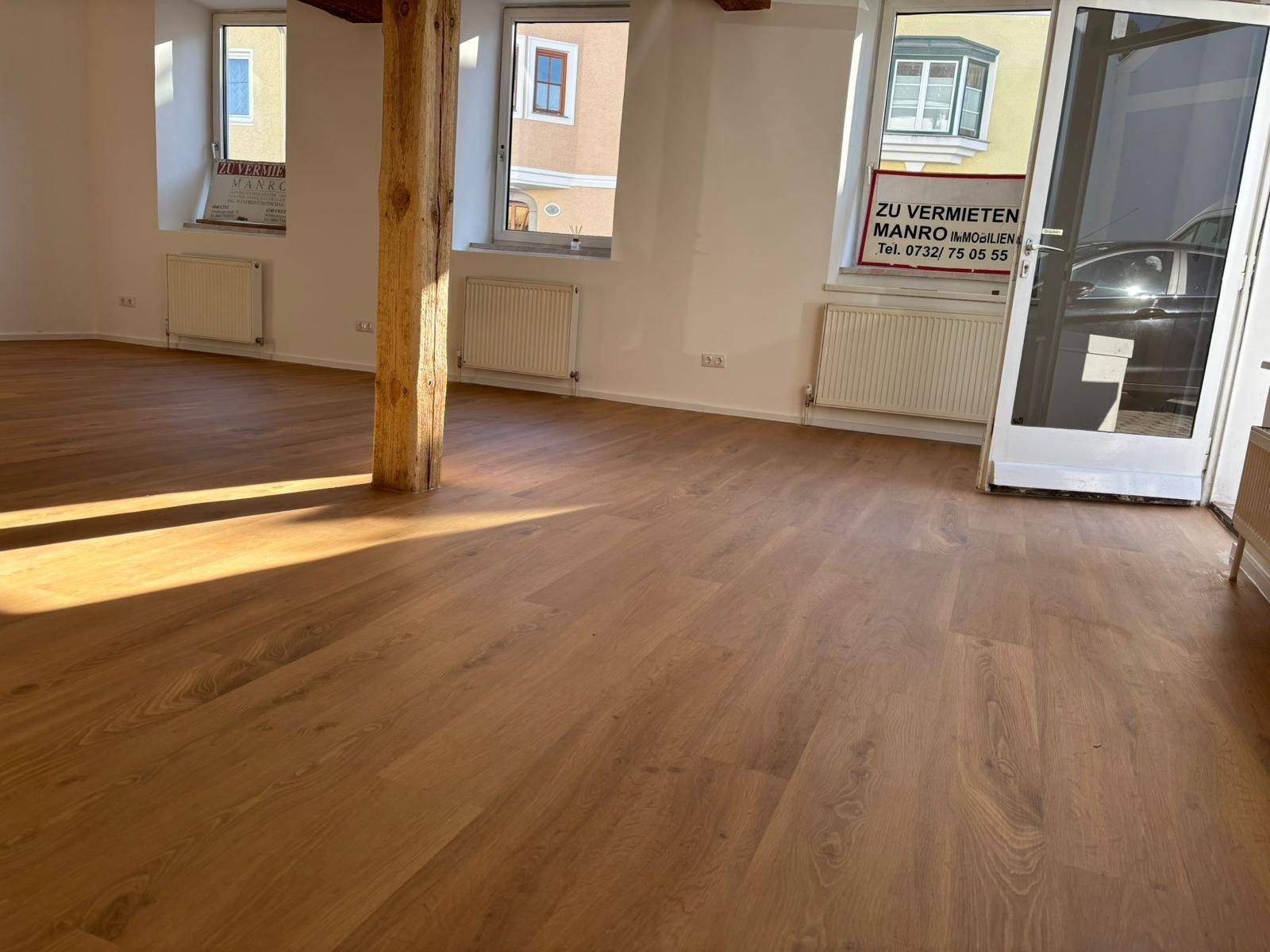 Heller Innenraum mit Holzboden, sichtbaren Holzbalken und Fenstern mit Blick auf die Umgebung.