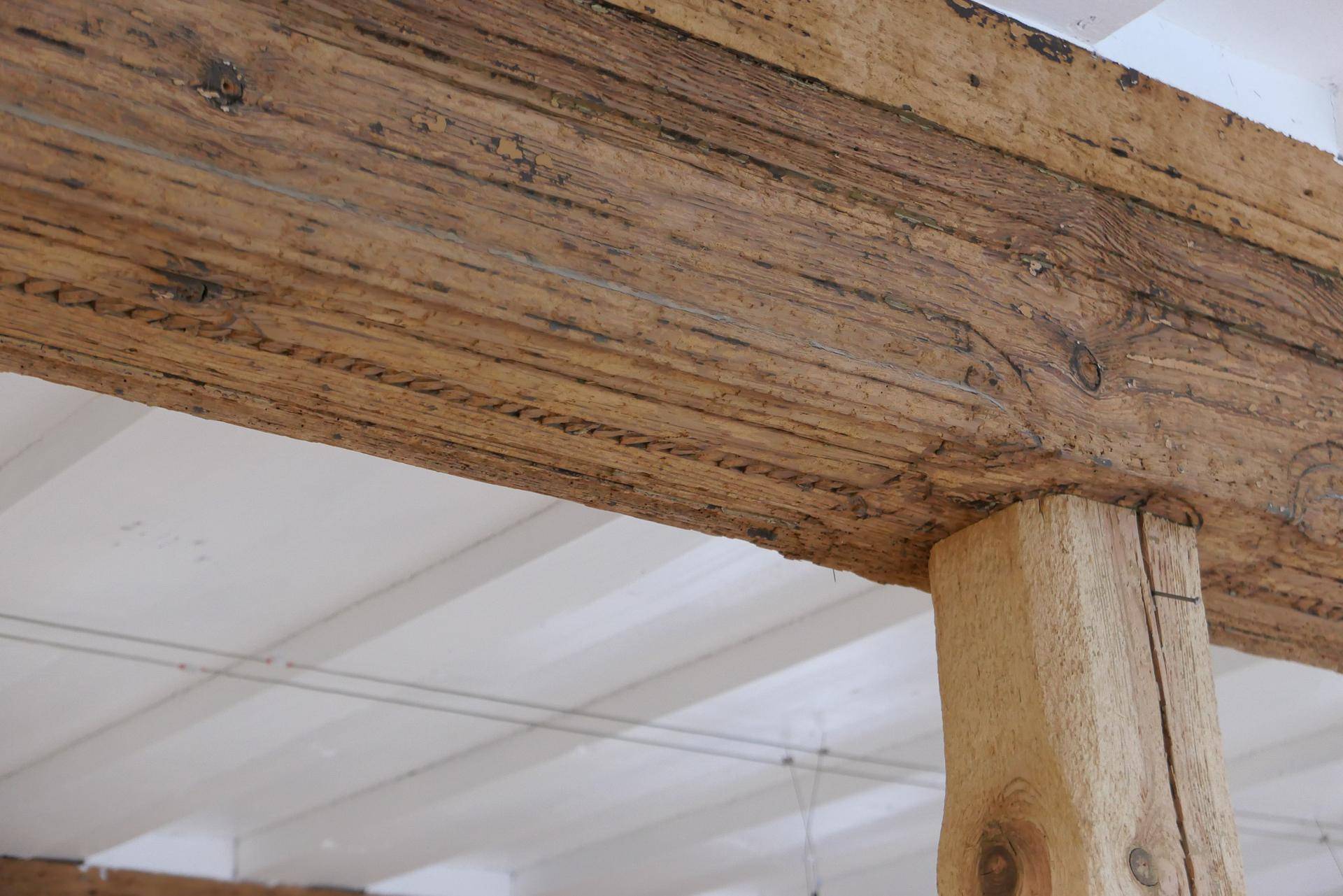 Nahaufnahme eines robusten Holzbalkens, der eine Holzdecke stützt, mit sichtbarer Maserung und Textur.