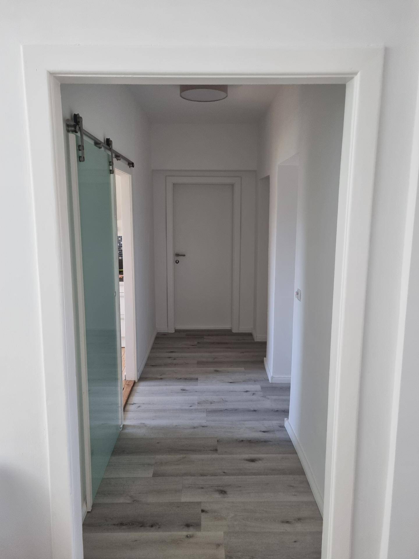 Heller Flur mit Laminatboden und einer modernen Glasschiebetür, die zu einem weiteren Raum führt.