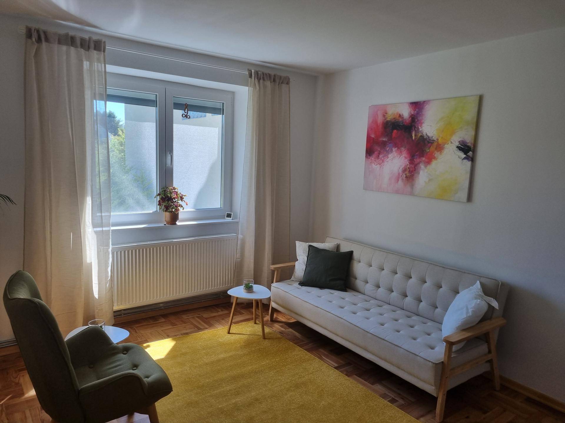 Heller Raum mit beigem Sofa, gelbem Teppich und einem großen Fenster, das viel Tageslicht hereinlässt.