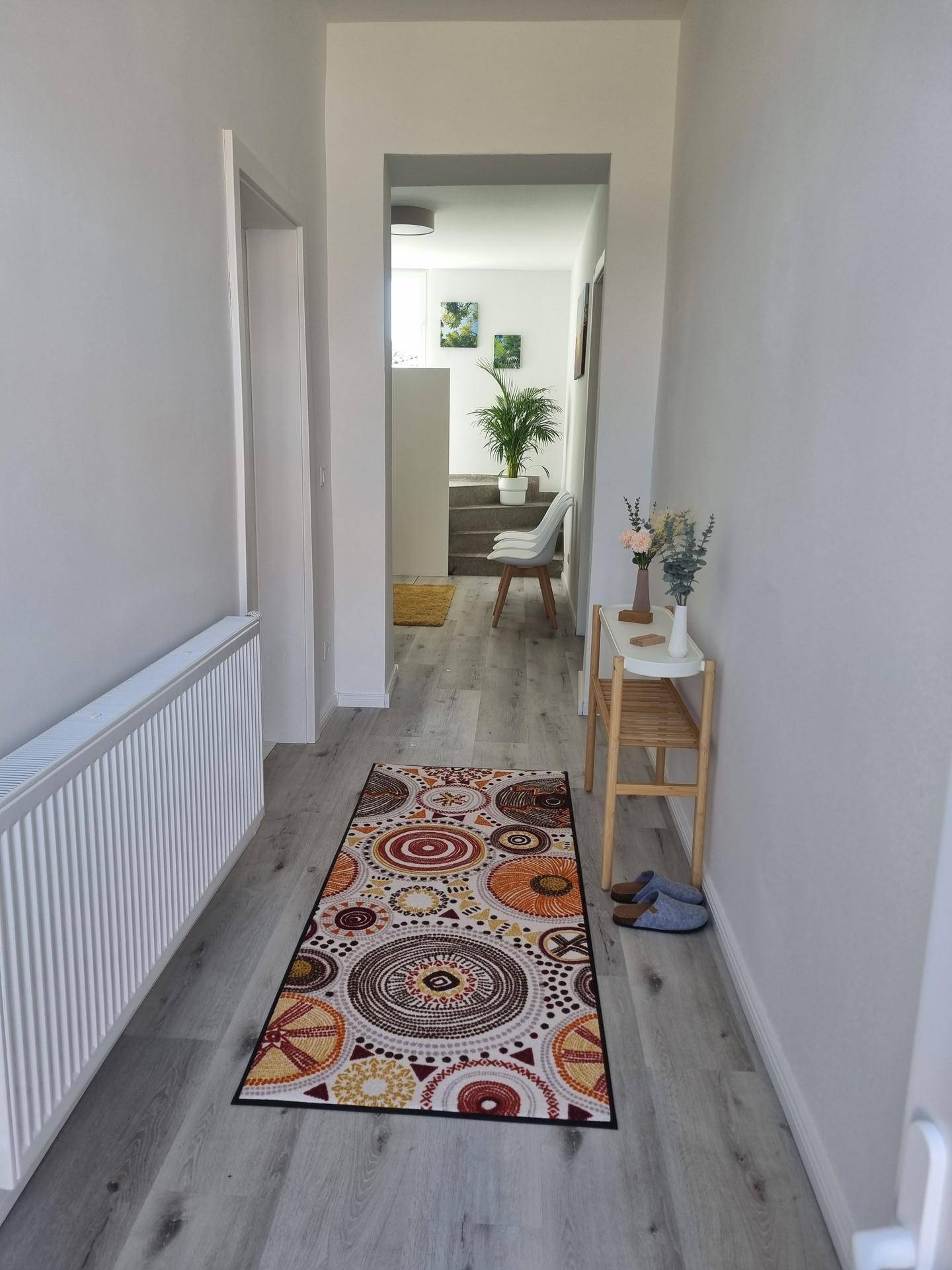Langer, heller Flur mit modernem Läufer, Laminatboden und Blick in einen weiteren Raum mit Treppe.
