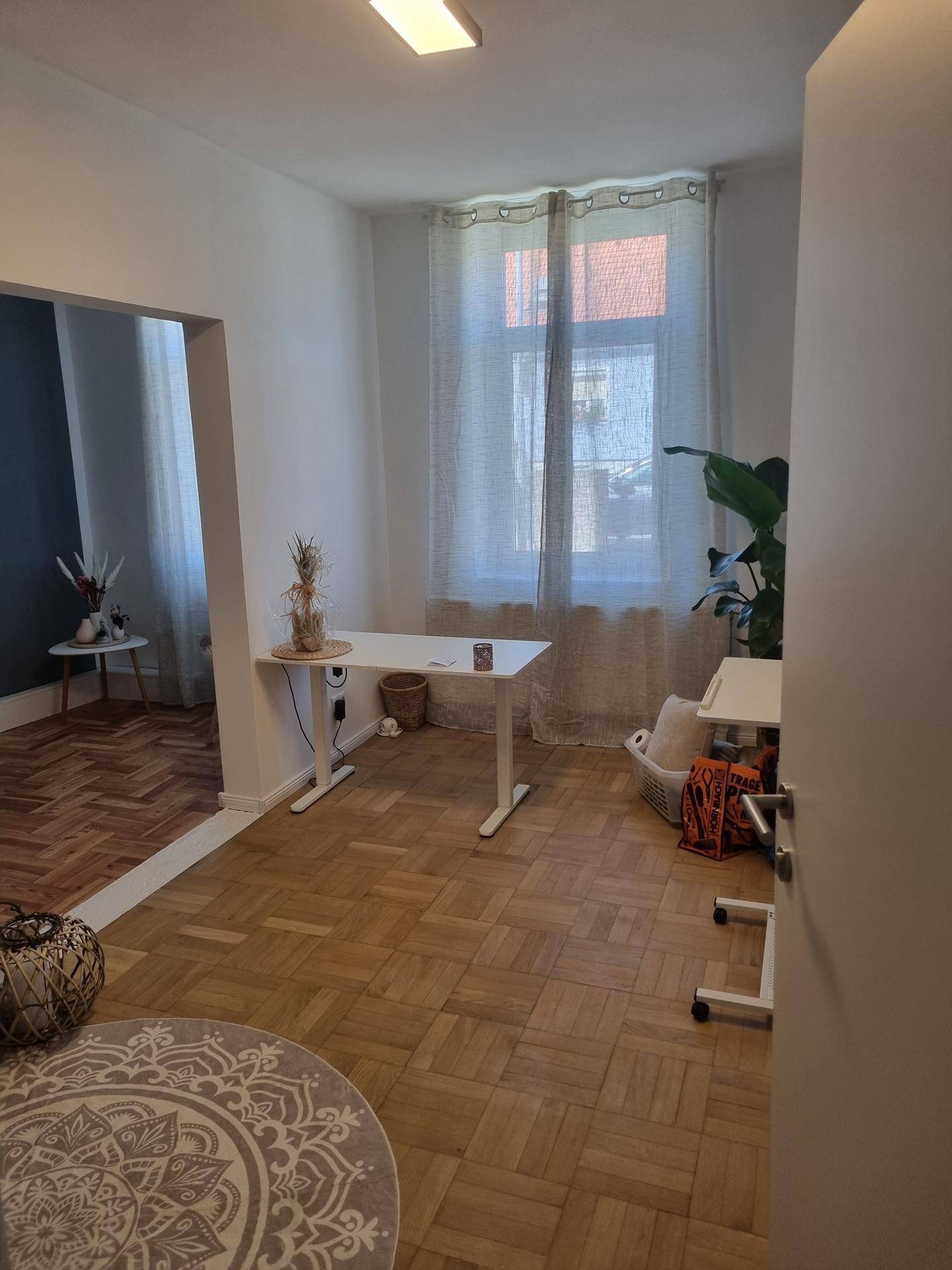 Helles Büro mit Fischgrätparkett, einem modernen Schreibtisch und Blick auf einen weiteren Raum.