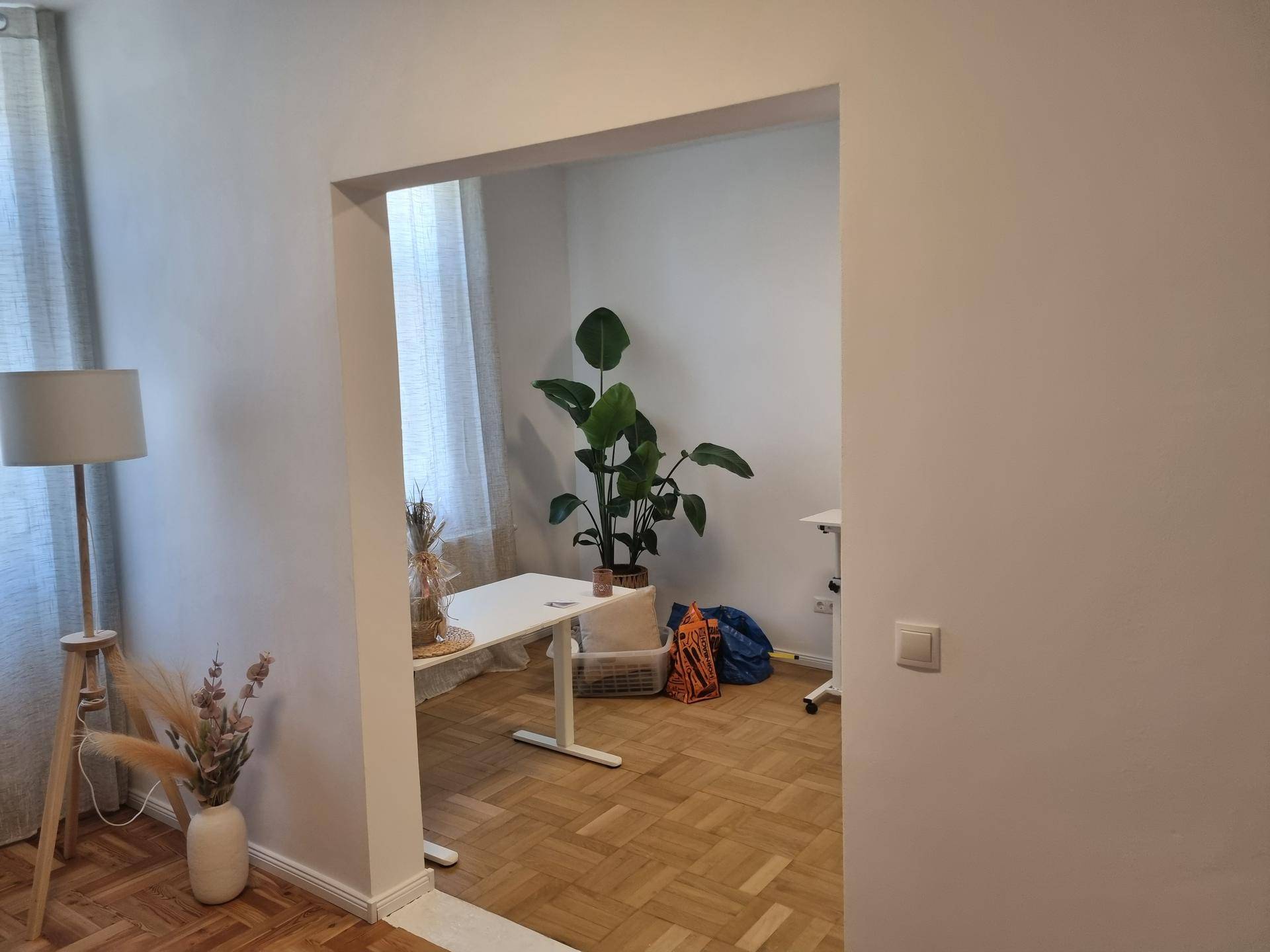 Offener Bürobereich mit Fischgrätparkett, einem modernen Schreibtisch und einer großen Grünpflanze.